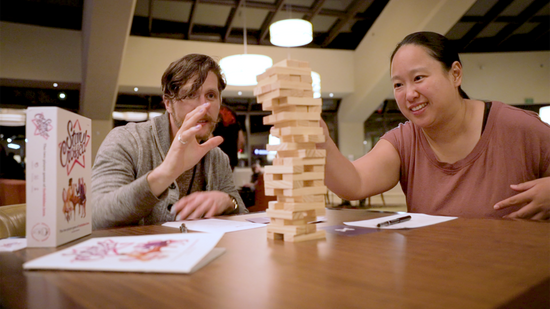 two players pulling bricks from a jenga tower, looking excited